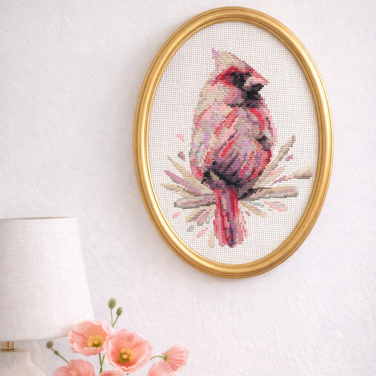 Framed female cardinal cross stitch artwork displayed in oval frame, finished counted cross stitch pattern featuring realistic pink cardinal bird design.
