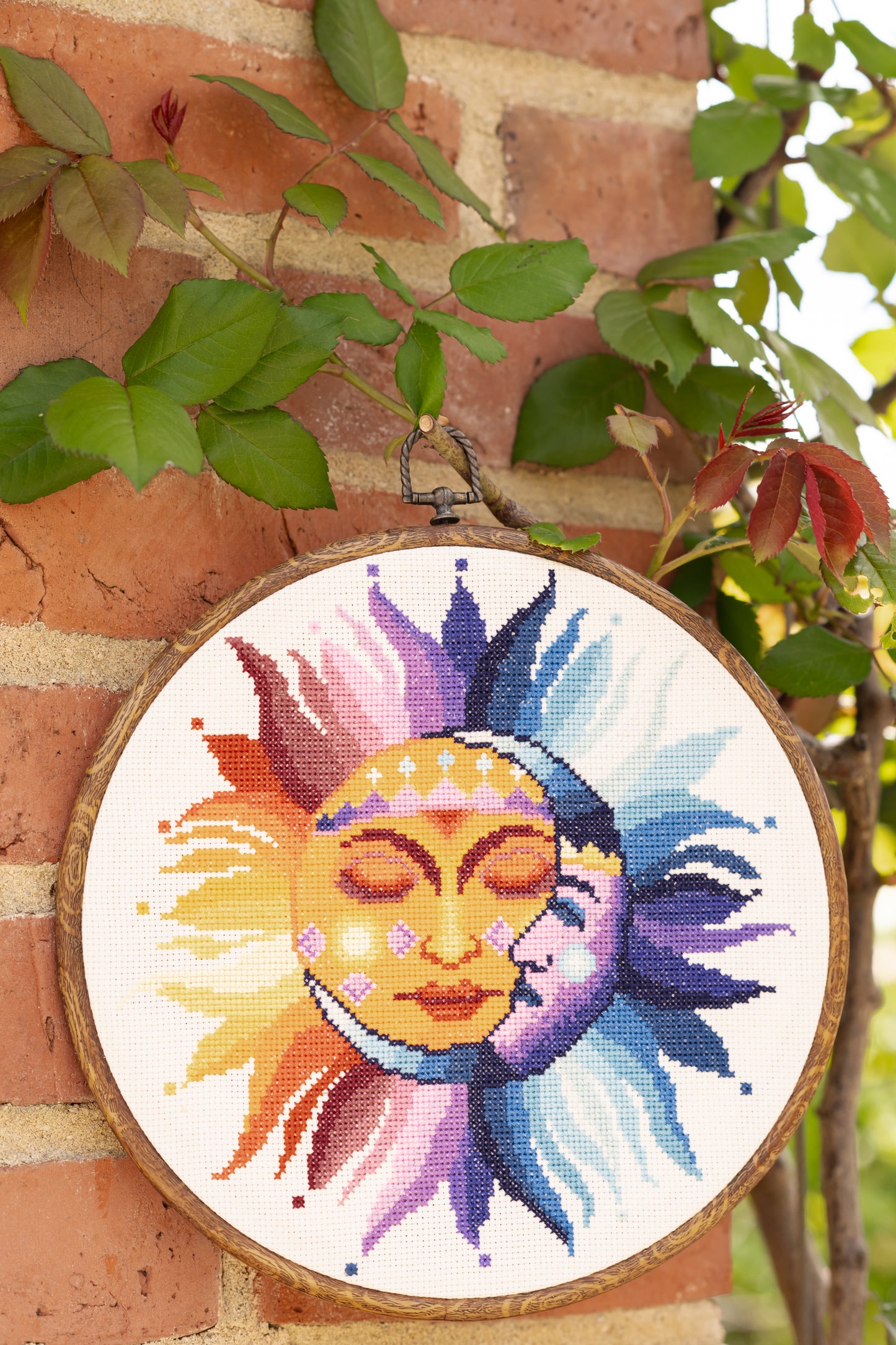 Colorful sun and moon design in a wooden hoop against a brick wall with greenery.