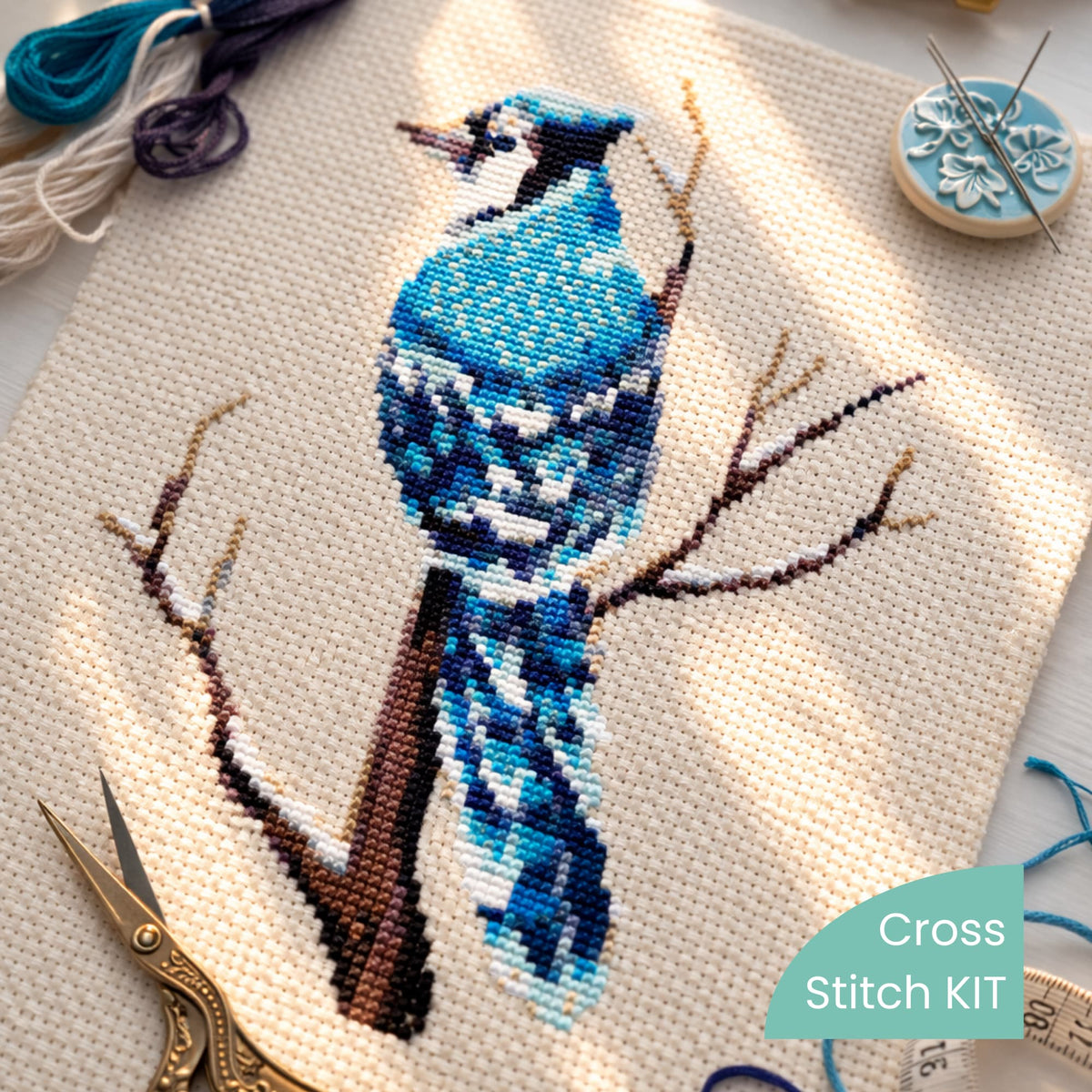 Blue Jay Counted Cross Stitch Kit with stitched bird design on Aida cloth, embroidery floss and scissors, modern bird needlework kit.