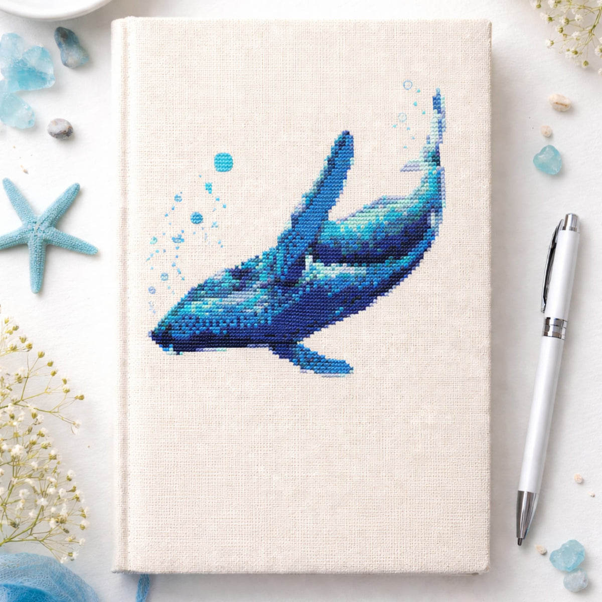 Blue Whale Counted Cross Stitch Kit displayed on linen notebook cover, whale embroidery kit, ocean themed needlework set for marine life lovers.