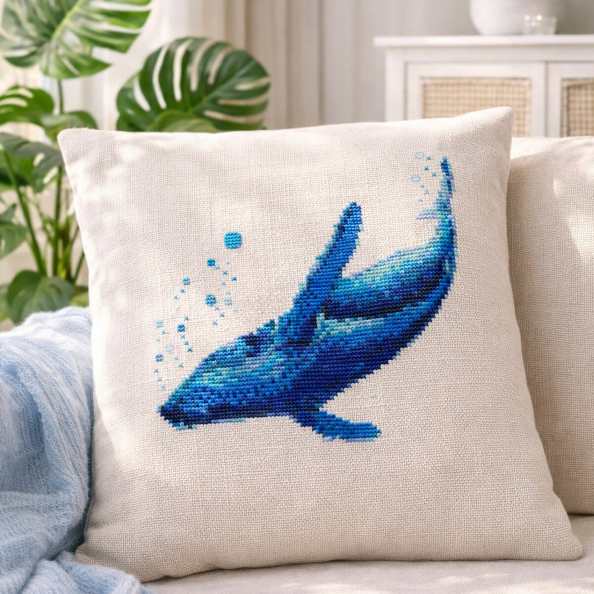 Blue Whale Counted Cross Stitch Kit shown on decorative pillow, ocean whale embroidery kit, coastal needlework set for beach house decor.