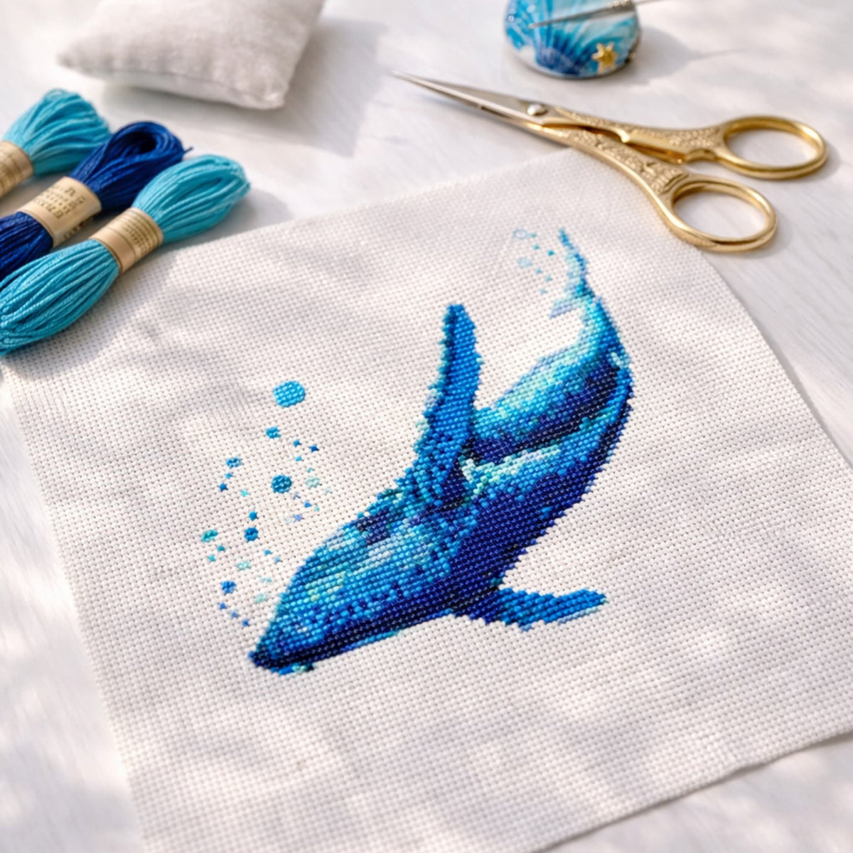 Blue Whale Counted Cross Stitch Kit with stitched whale design on white Aida cloth, blue floss and scissors, ocean embroidery kit for sea life lovers.
