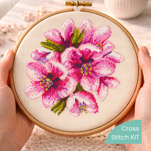 Cherry blossom cross stitch kit displayed in embroidery hoop held in hands, showing detailed pink floral design.