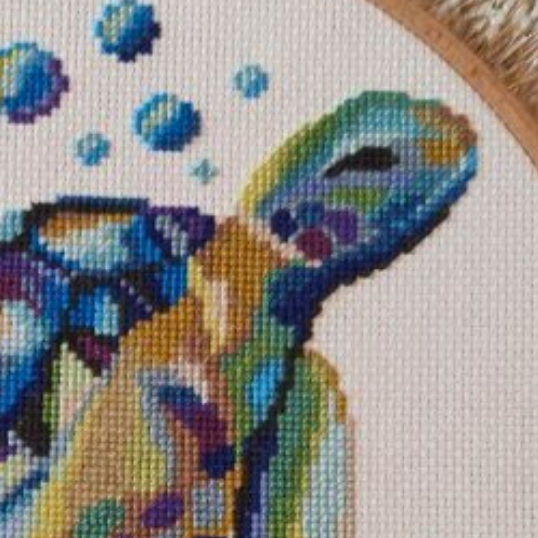 Close-up of colorful sea turtle cross stitch design showing detailed stitches and vibrant blue, green and purple threads