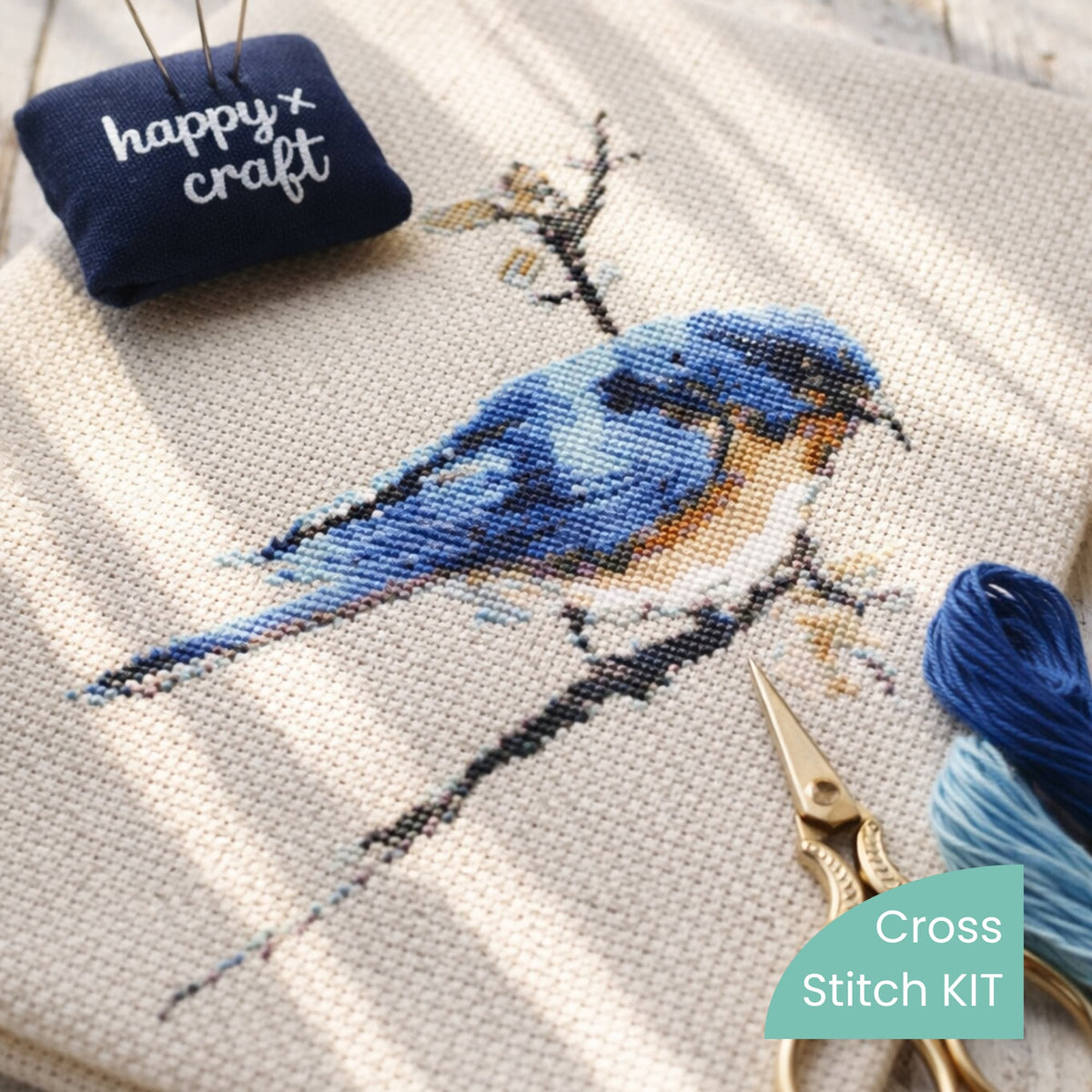 Close-up of finished blue bird cross stitch stitched on linen, shown as a finished example. Available as a complete cross stitch kit by Happy x Craft.