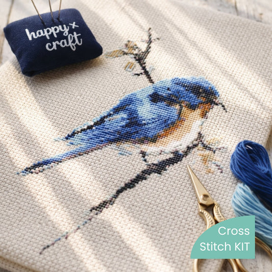 Close-up of finished blue bird cross stitch stitched on linen, shown as a finished example. Available as a complete cross stitch kit by Happy x Craft.