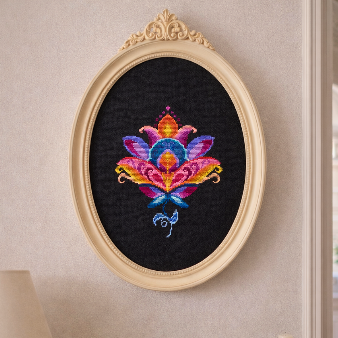 Colorful folk lotus cross stitch embroidery framed in an elegant oval frame, displayed as wall art on a light interior wall.