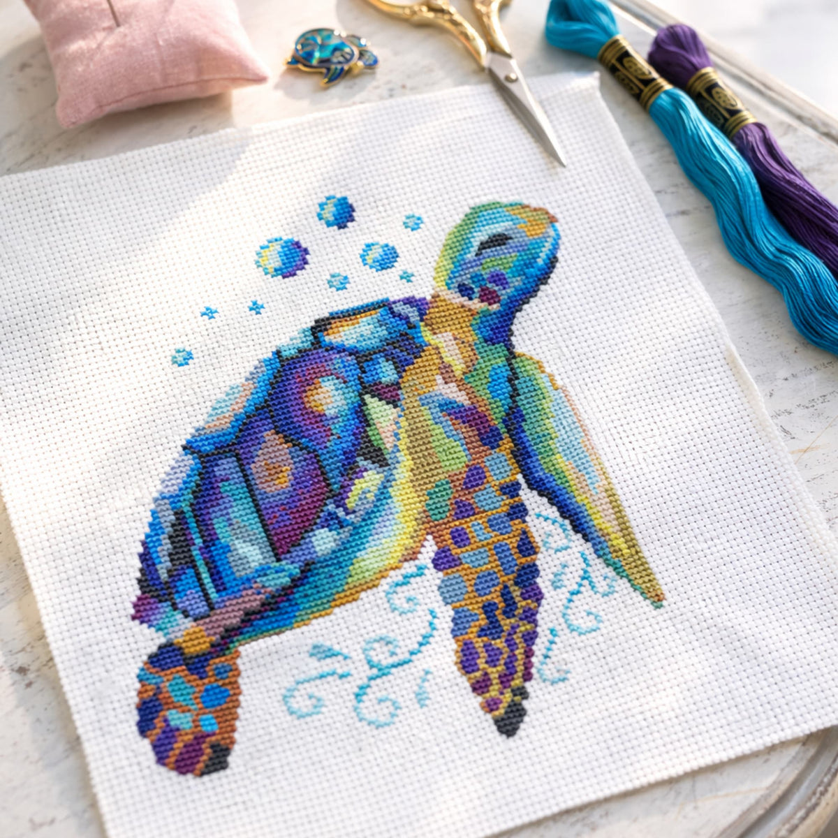 Cross-stitched colorful turtle design on fabric with embroidery tools in the background