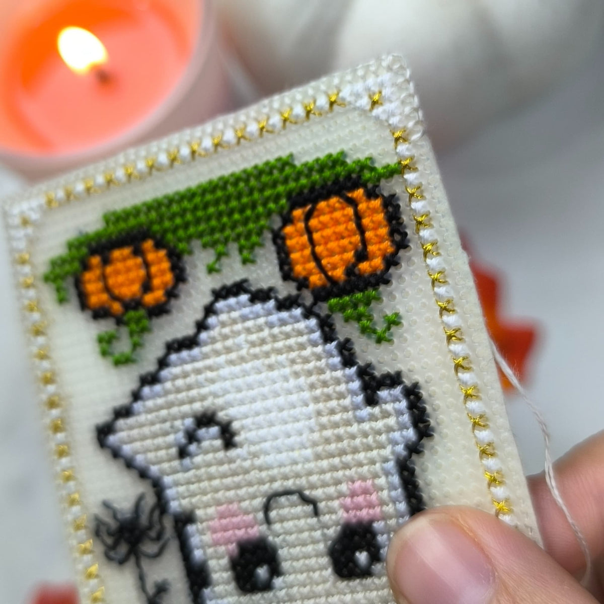 Cross-stitched ghost with pumpkins and spider on a white background