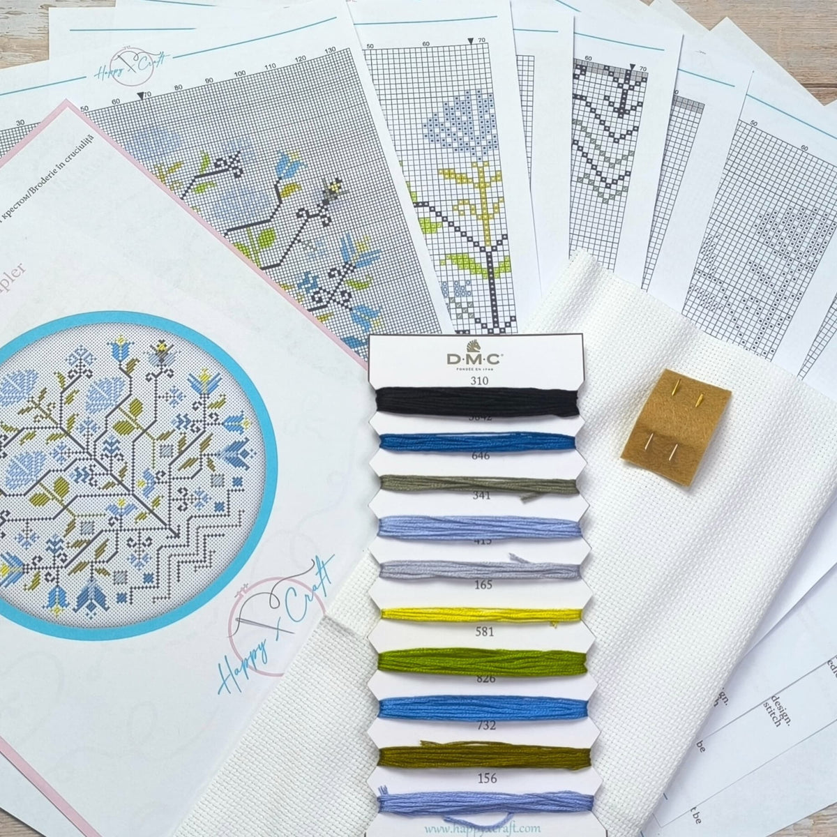 Cross stitch kit Blue Flowers Sampler displayed with printed color charts, DMC embroidery threads, white Aida fabric, and needle set. The image shows all included materials needed to stitch the finished floral sampler design. 