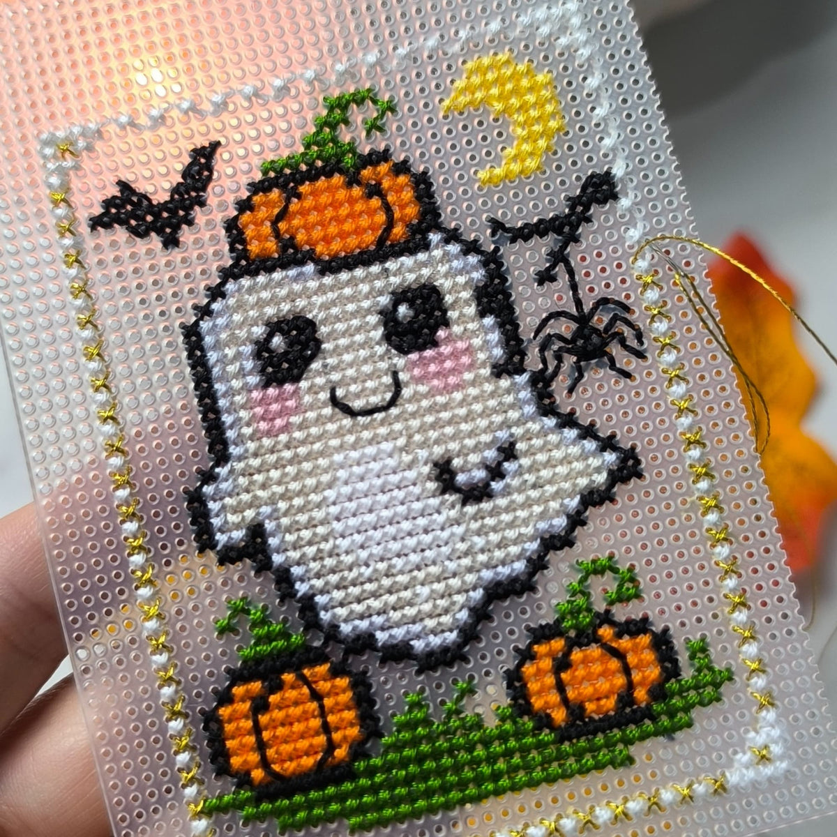 Cross-stitched ghost with pumpkins and spider on a white background