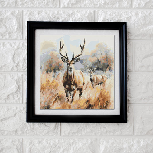 A framed cross stitch pattern depicting a deer in a savanna landscape, displayed on a wall