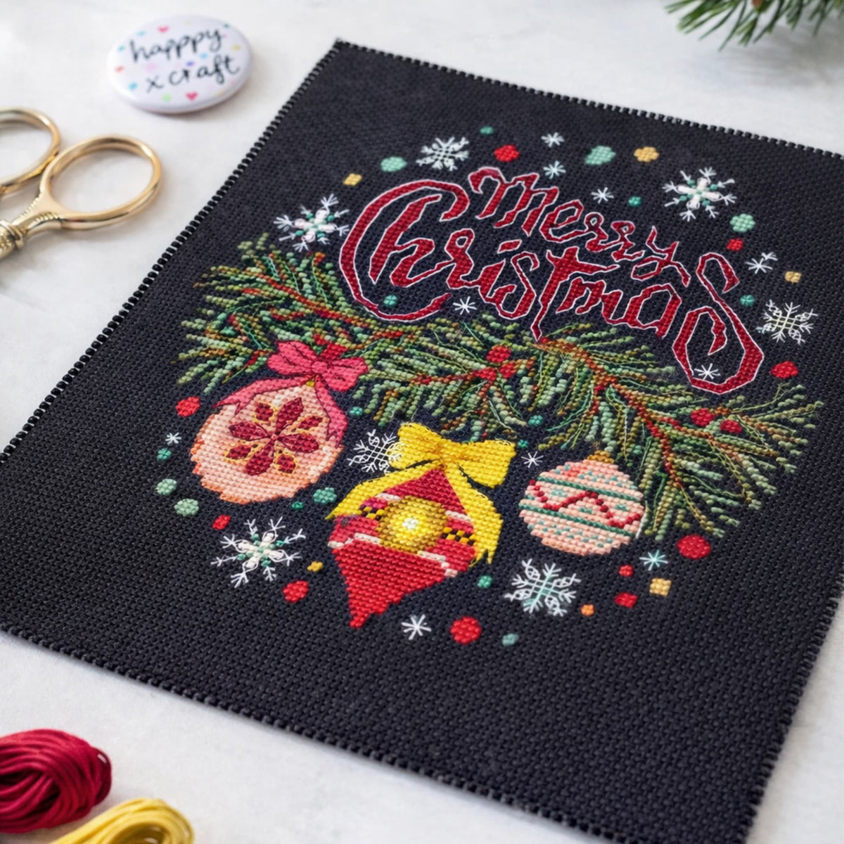 Digital cross stitch pattern Merry Christmas shown as flat lay embroidery piece with scissors and thread