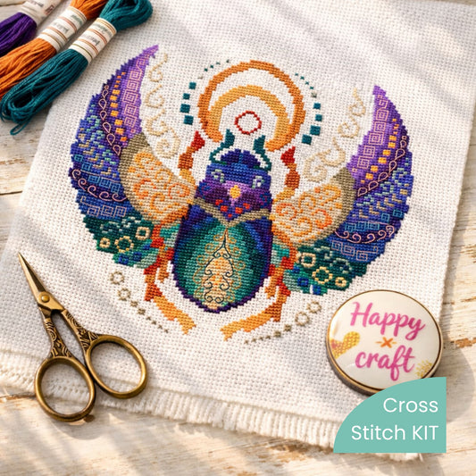 Egyptian scarab bug cross stitch kit flat lay with embroidery threads, scissors and needle on white fabric