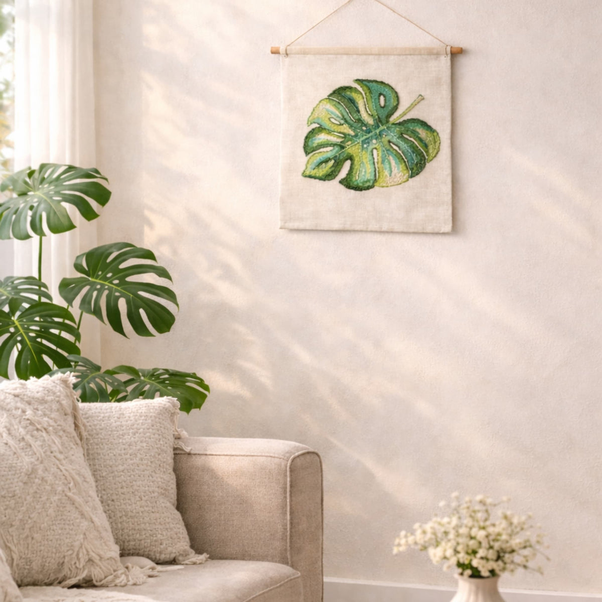 Monstera leaf cross stitch kit displayed as wall hanging in modern living room, tropical botanical decor.