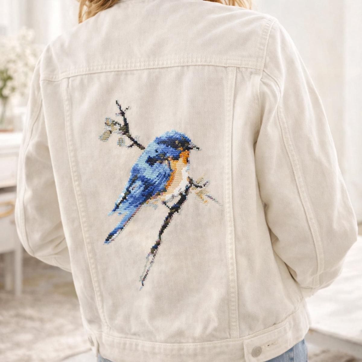 Finished blue bird cross stitch on the back of a jacket, shown as an example of the completed design included in the cross stitch kit.