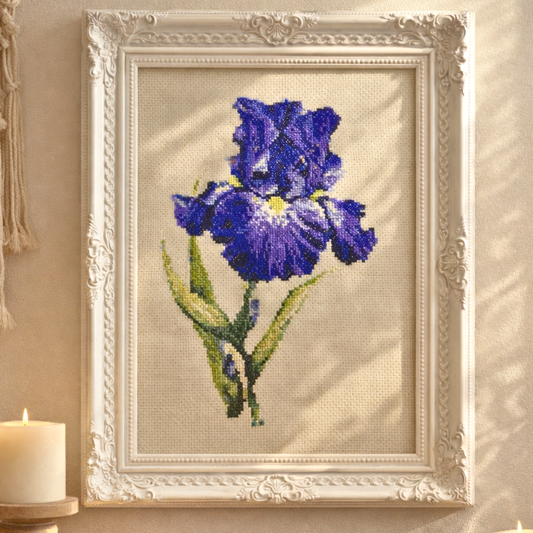 Framed purple blue iris cross stitch artwork displayed as elegant floral wall decor with classic white frame