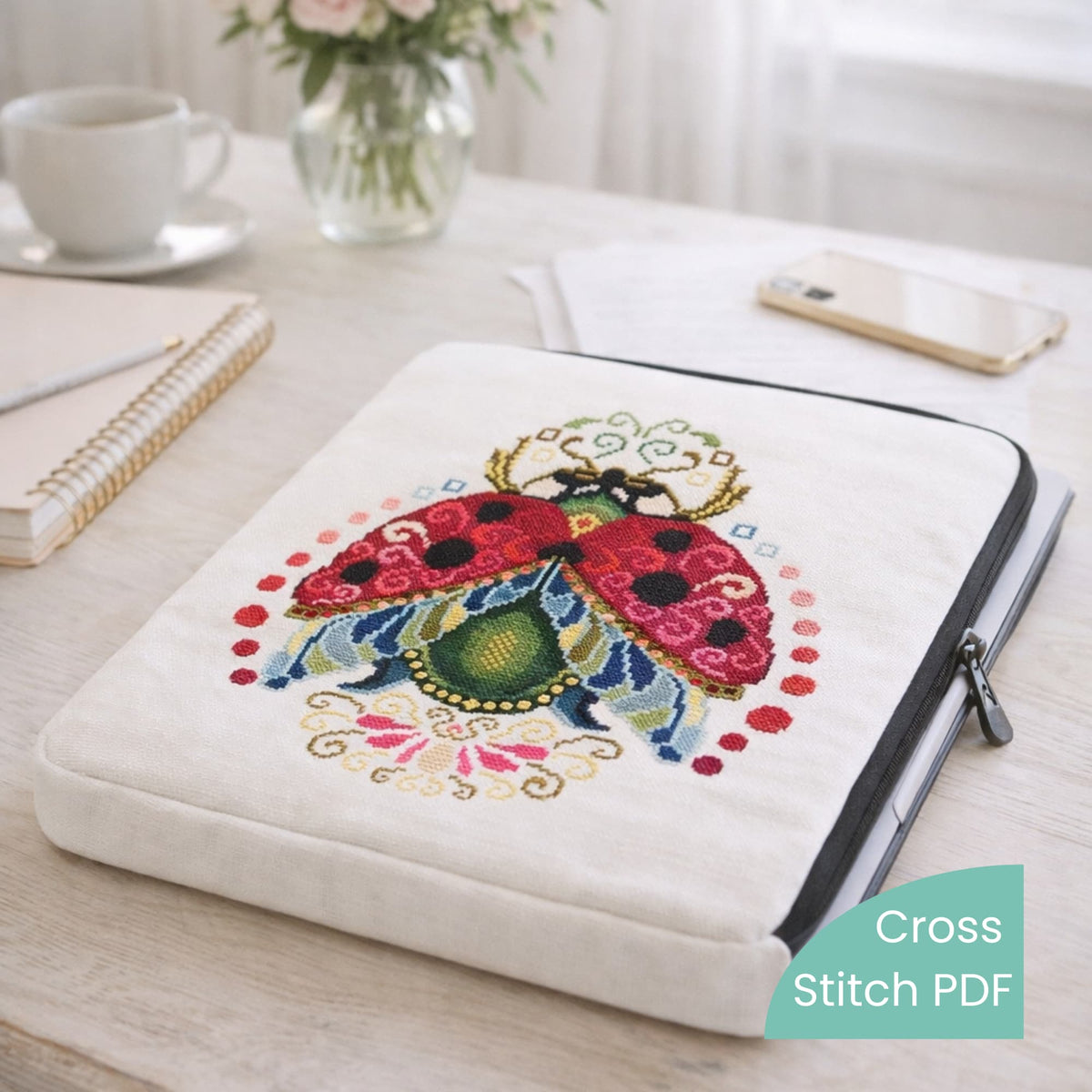 Ladybug cross stitch embroidery on linen laptop sleeve, colorful folk style ladybug design stitched on tablet or laptop protective cover, handmade embroidery inspired accessory.