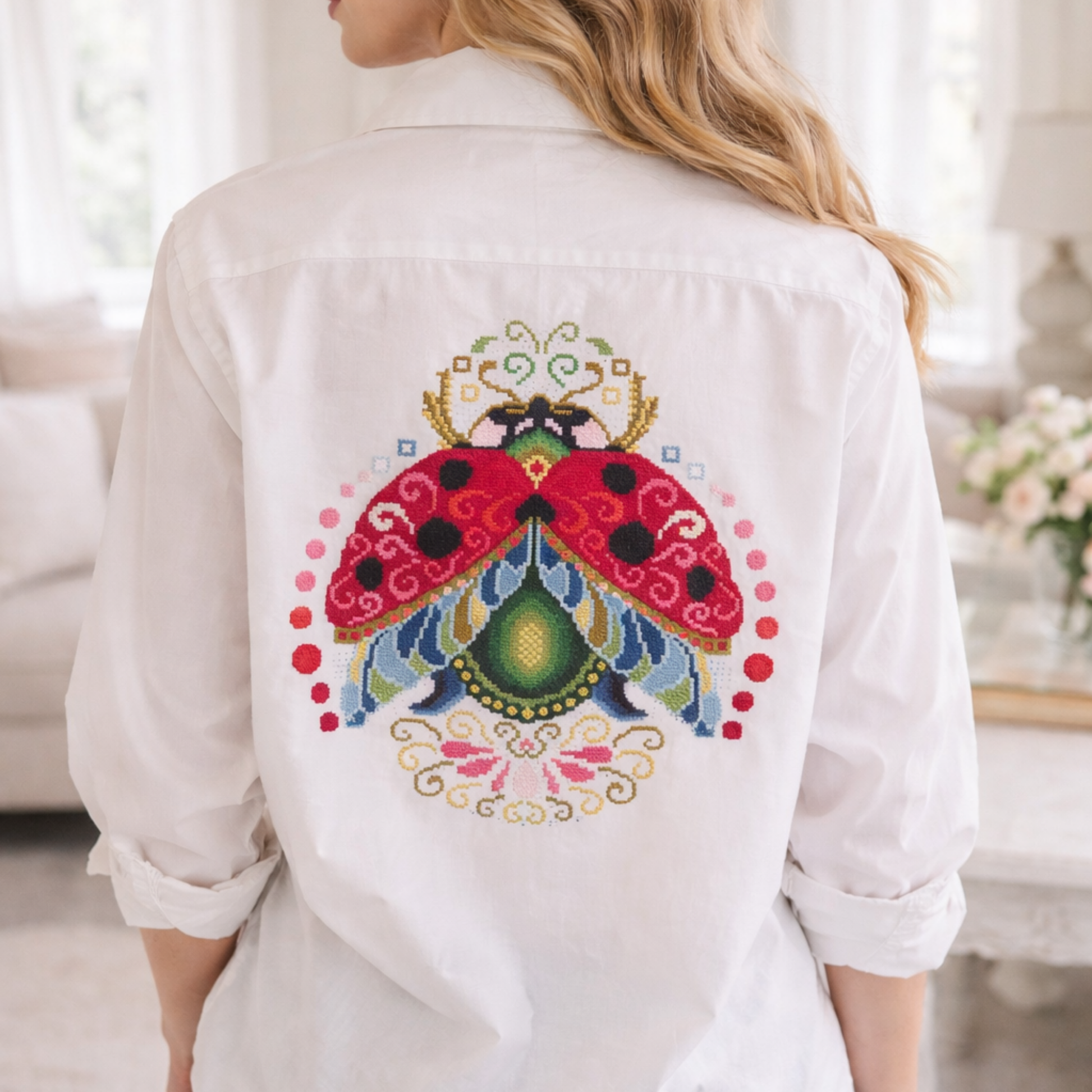Large ladybug cross stitch embroidery on white shirt back, detailed folk inspired ladybug design, handmade decorative embroidery on clothing, Eastern European embroidery style.