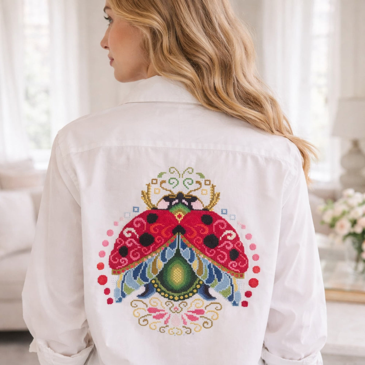 Large ladybug cross stitch embroidery on white shirt back, detailed folk inspired ladybug design, handmade decorative embroidery on clothing, Eastern European embroidery style.