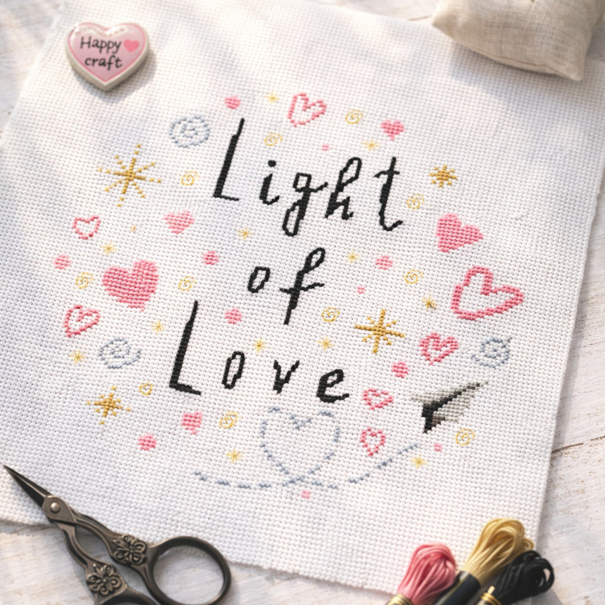 Light of Love cross stitch pattern PDF displayed as flat lay embroidery with pink hearts and gold stars with embroidery tools