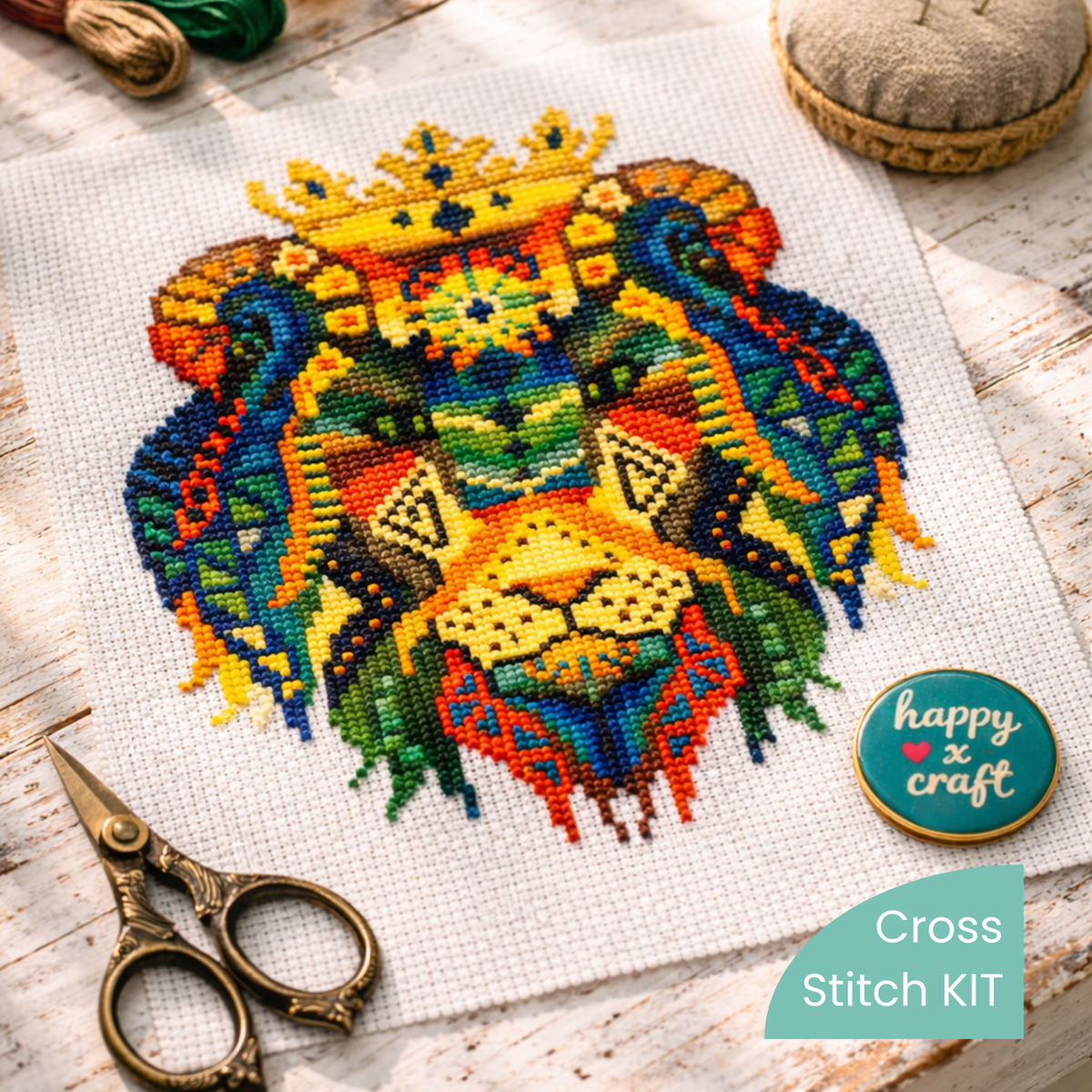 Lion King cross stitch kit contents showing stitched crowned lion design on Aida fabric with embroidery scissors, threads, and sewing accessories displayed on rustic wooden table.