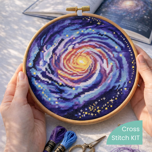 Milky Way Galaxy Counted Cross Stitch Kit stitched in embroidery hoop held in hands, spiral galaxy embroidery kit, cosmic needlework set.
