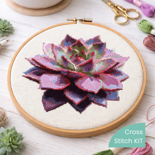 Purple Succulent Counted Cross Stitch Kit displayed in embroidery hoop with embroidery threads, scissors and succulent plants.