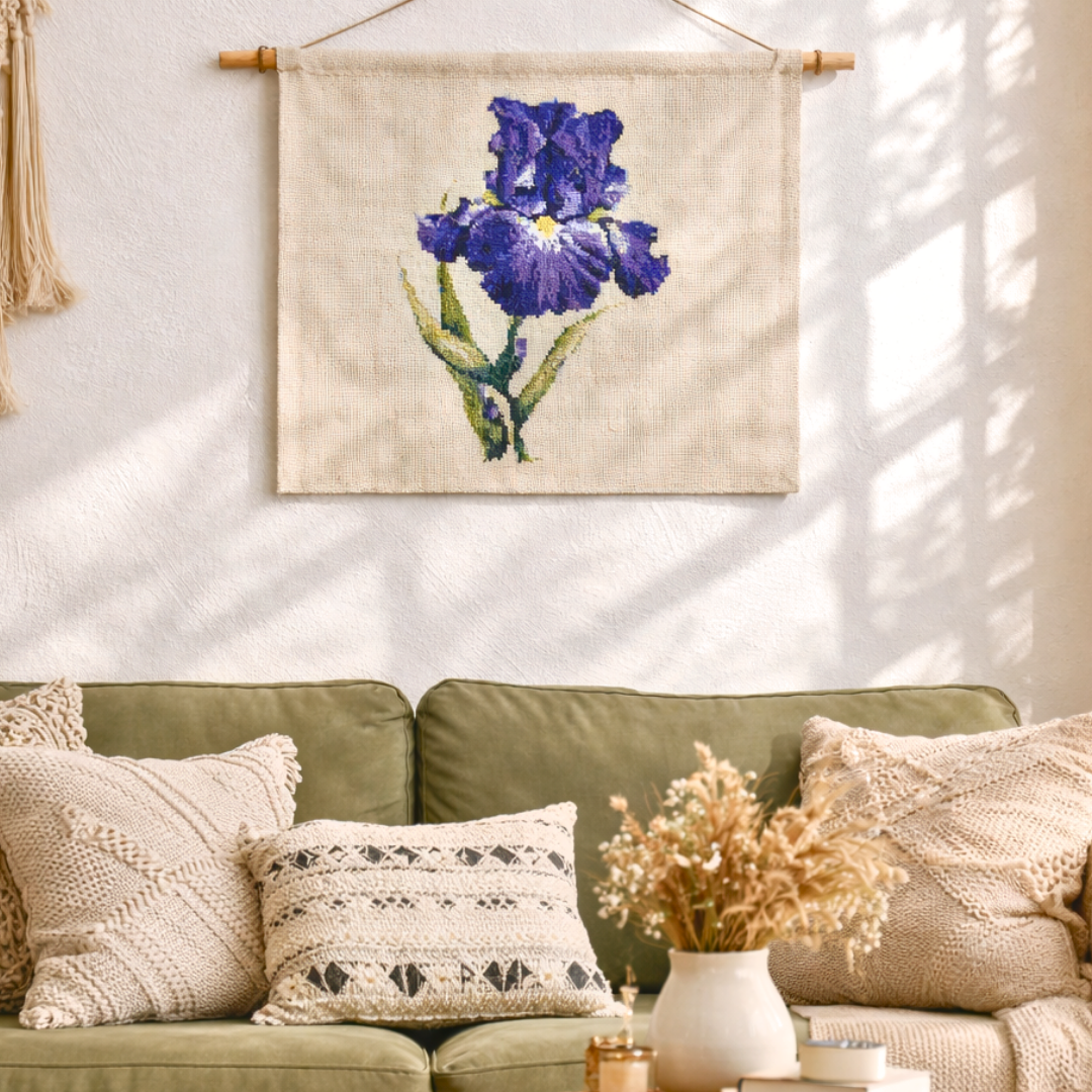 Purple blue iris cross stitch wall hanging displayed as textile art on a neutral wall with soft natural light