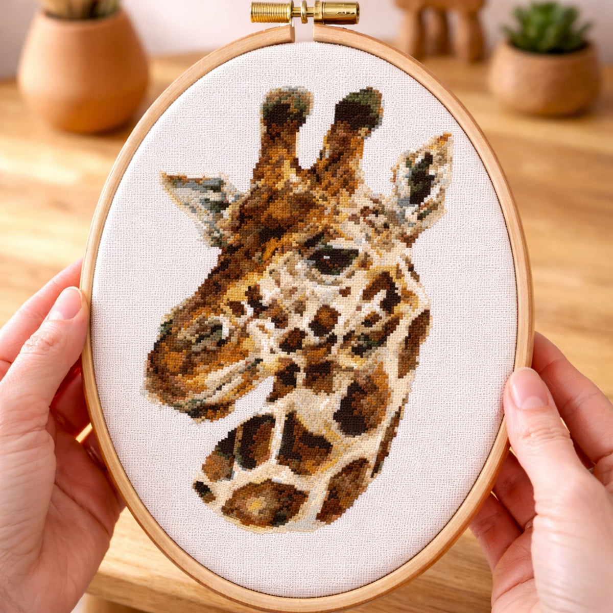 Realistic giraffe counted cross stitch kit displayed in embroidery hoop held in hands with detailed animal design.