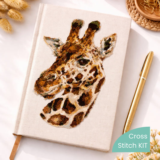 Realistic giraffe counted cross stitch kit displayed on notebook cover with detailed safari animal embroidery design.