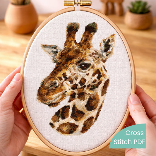 Realistic giraffe cross stitch pattern PDF displayed in embroidery hoop held in hands with detailed animal design.