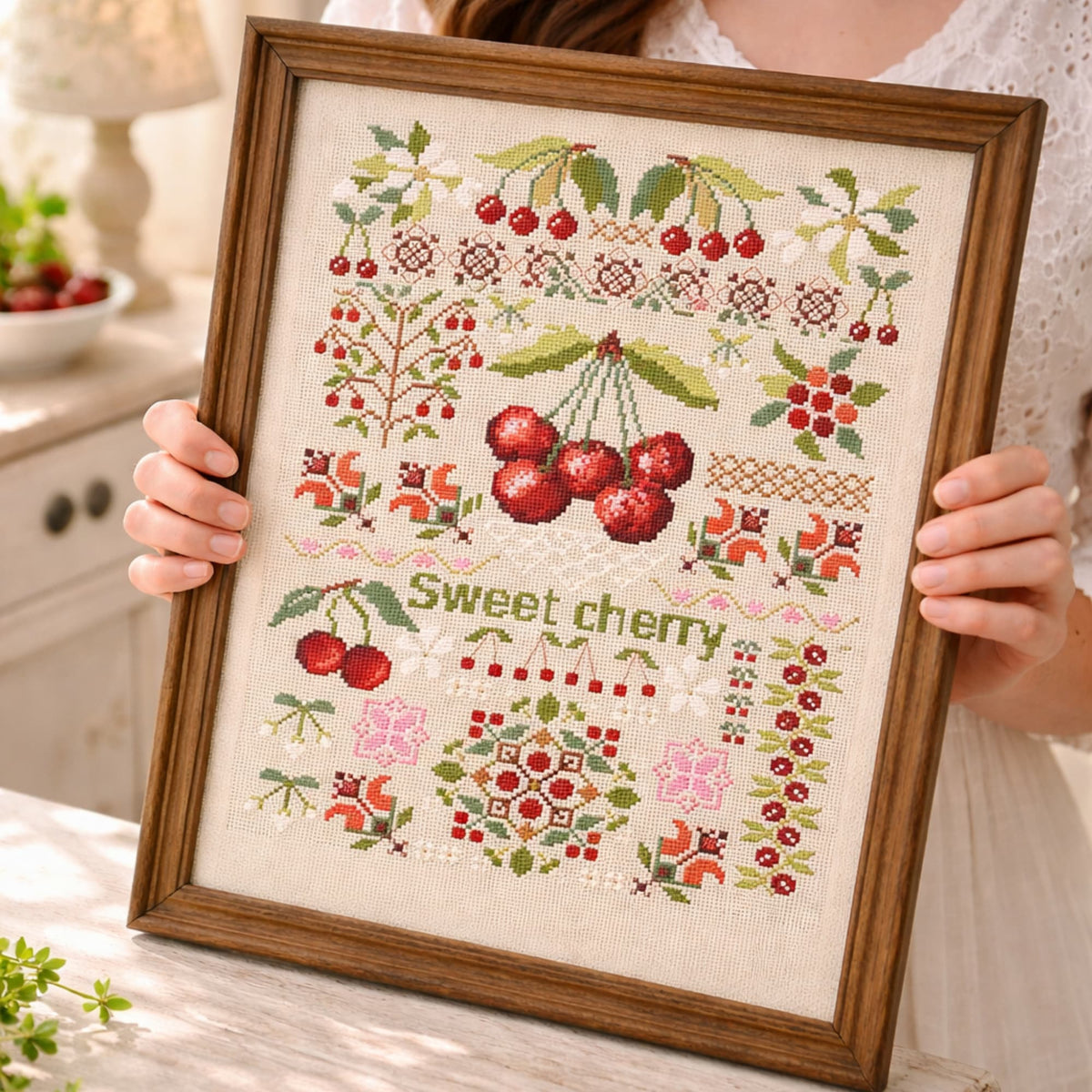 Sweet cherry cross stitch kit held in frame displaying detailed botanical fruit sampler embroidery design.