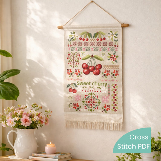 Sweet cherry cross stitch pattern PDF displayed as finished wall hanging with botanical fruit sampler embroidery design.