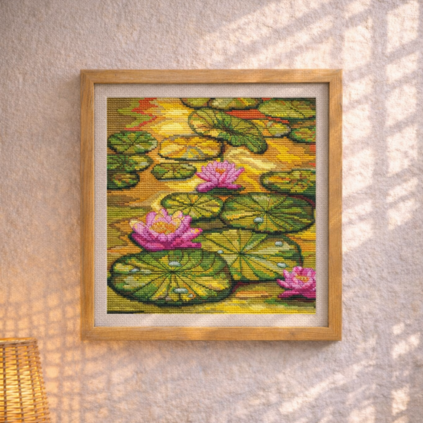 Framed cross-stitched artwork of water lilies on a textured wall.