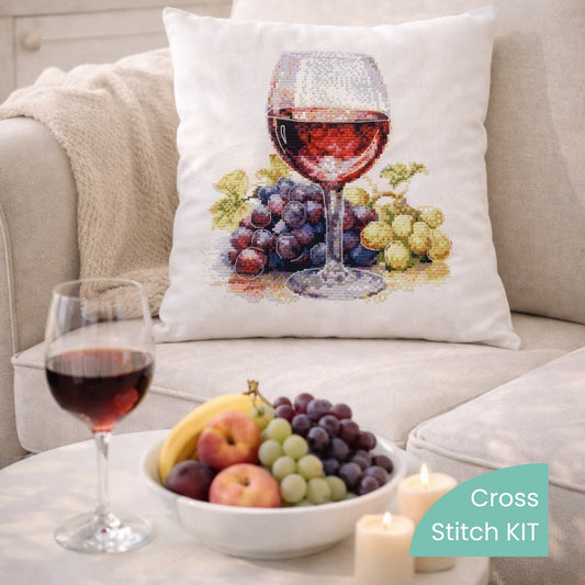 Wine glass and grapes cross stitch kit displayed on decorative pillow, realistic wine still life DIY embroidery project