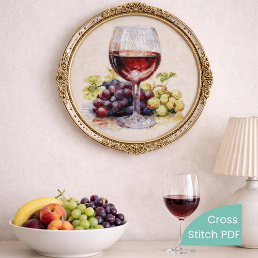 Wine glass and grapes cross stitch pattern PDF displayed in decorative frame on wall, realistic still life embroidery design
