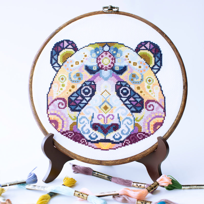 Folk modern panda counted cross stitch kit displayed in embroidery hoop and threads with detailed colorful panda design ready for stitching.